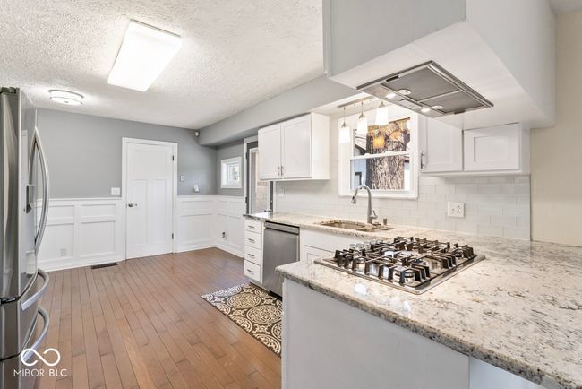 kitchen featuring white cabinetry, wainscoting, hardwood / wood-style floors, stainless steel appliances, and a sink | Image 10