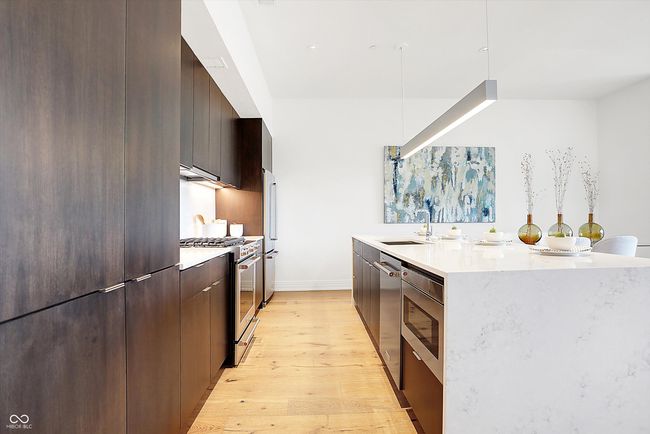 The kitchen has a pantry, large center island with walnut drawers and cabinets, refrigerator, gas stove with convection and steam bake options, dishwasher, drawer microwave and a beautiful quartz waterfall countertop | Image 9
