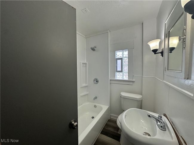 Full bath featuring a sink, a textured ceiling, toilet, shower / bathtub combination, and wood finished floors | Image 25