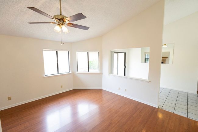Empty room with vaulted ceiling, ceiling fan, a textured ceiling, wood finished floors, and baseboards | Image 13