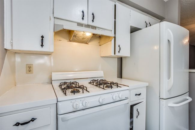 Kitchen with light countertops, white cabinetry, under cabinet range hood, and white appliances | Image 11