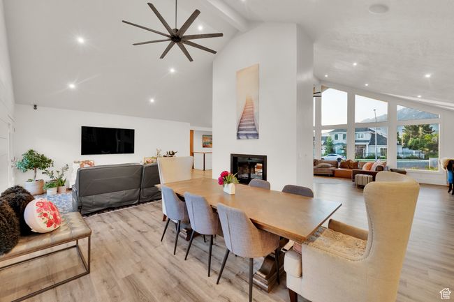Dining space featuring high vaulted ceiling, a fireplace, a ceiling fan, light wood-type flooring, and beam ceiling | Image 8