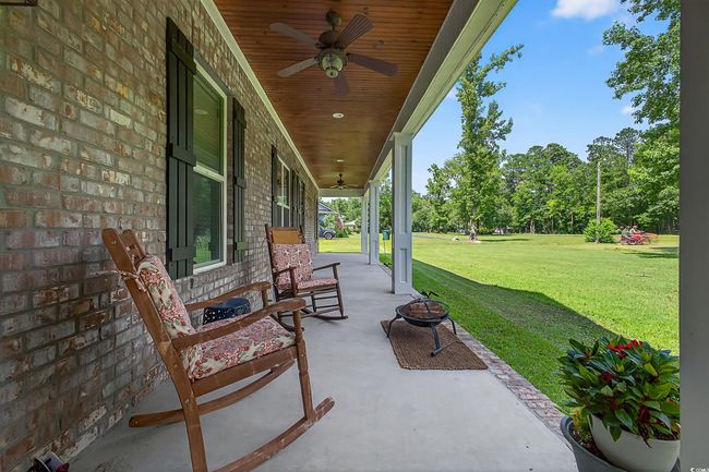 Covered porch featuring a ceiling fan, a lawn, a fire pit, and view of wooded area | Image 6