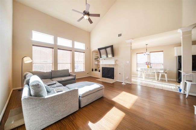 Living room featuring a ceiling fan, a tiled fireplace, wood finished floors, high vaulted ceiling, and a chandelier | Image 17