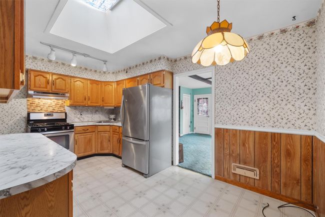 Kitchen featuring under cabinet range hood, stainless steel appliances, a skylight, light floors, and wallpapered walls | Image 10