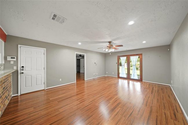 Photo shows the living area with double doors that lead to the backyard. White closed door leads to the 2 car garage and the open door leads to the primary bedroom. | Image 10