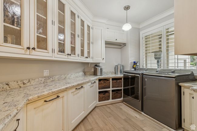 Kitchen featuring independent washer and dryer, light wood-style floors, crown molding, hanging light fixtures, and glass insert cabinets | Image 22
