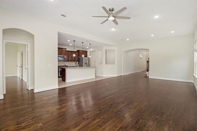 Spacious open-concept living area with rich hardwood floors and ample natural light. The kitchen features modern stainless steel appliances, pendant lighting, and a large island. Neutral walls and recessed lighting enhance the airy feel. | Image 6