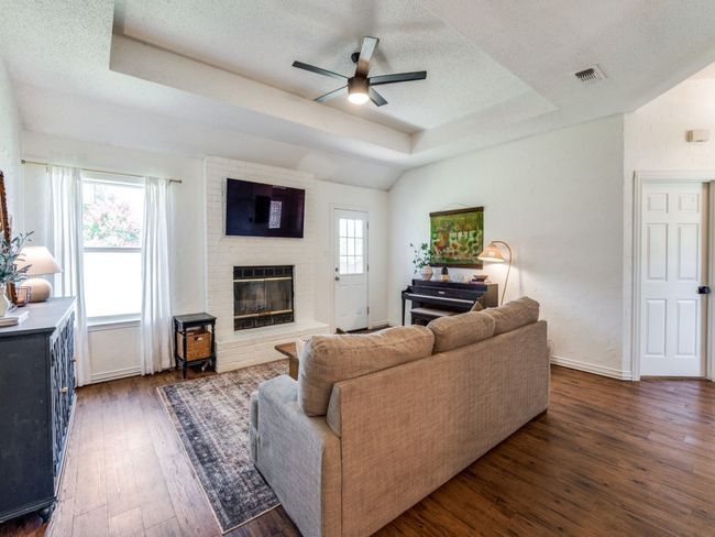 Living room featuring a raised ceiling, wood-type flooring, ceiling fan, a fireplace, and a textured ceiling | Image 8