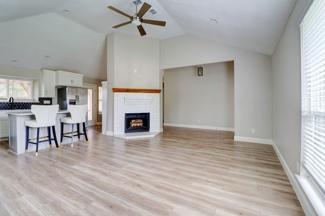 Living area with ceiling fan, vaulted ceiling, a brick fireplace, and light wood finished floors | Image 5