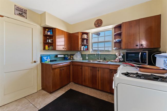 Kitchen featuring brown cabinets, open shelves, stainless steel microwave, a sink, and white range with gas stovetop | Image 8