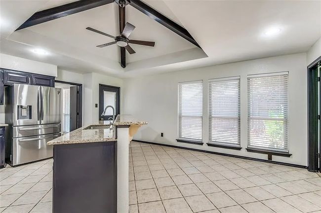 Kitchen with light stone counters, light tile patterned flooring, a sink, stainless steel refrigerator with ice dispenser, and a raised ceiling | Image 15
