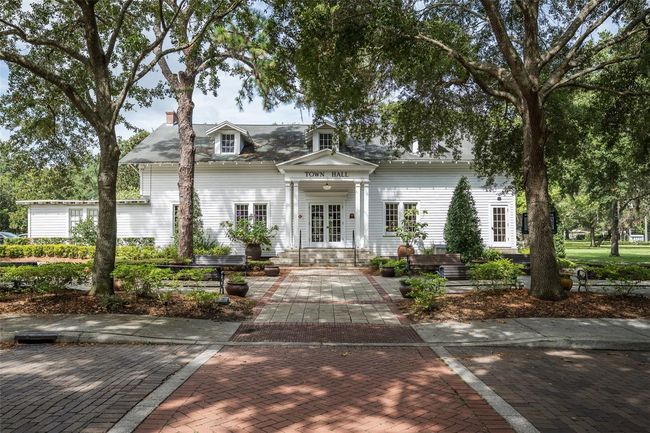 This is the historic Windermere Town Hall, a beloved landmark nestled under the shade of towering oak trees in the heart of downtown Windermere. With its classic white clapboard exterior, charming dormer windows, and inviting front porch, the Town Hall reflects the timeless character and small-town charm that define this Central Florida community. Surrounded by brick walkways and peaceful park benches, it’s not just the hub for town meetings—it’s a gathering place for local events, weddings, and neighborhood celebrations. A symbol of Windermere’s rich heritage and close-knit spirit, this picturesque building captures the essence of life in one of Florida’s most desirable towns. | Image 39