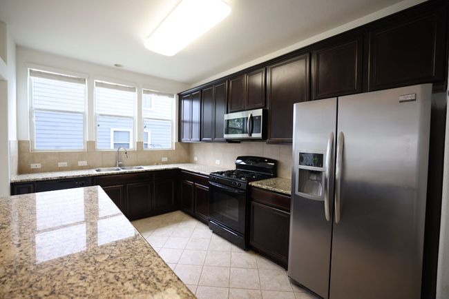 The kitchen features granite counters, stainless appliances, tall 48” cabinets, and an oversized island built for gathering. | Image 9