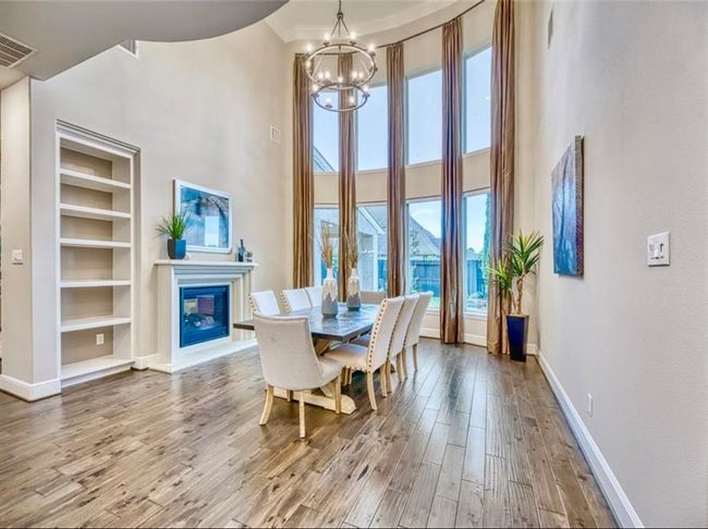 This dining area features high ceilings and large windows with elegant drapes, providing abundant natural light. It includes a modern chandelier, built-in shelves, a fireplace, and hardwood floors, creating a stylish and inviting space. | Image 12