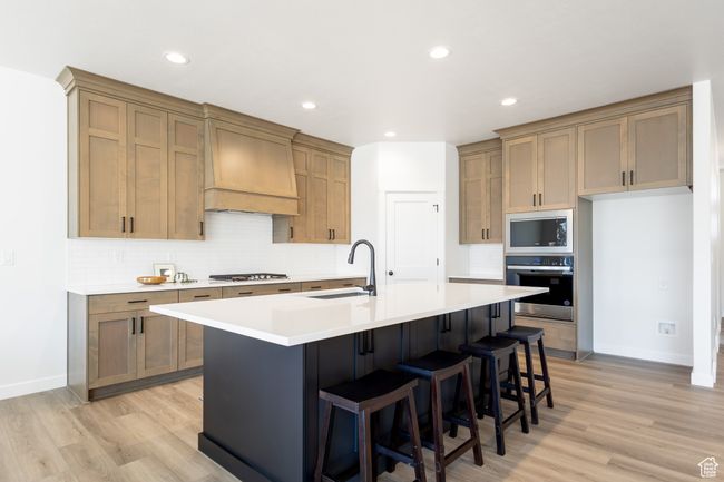 Kitchen featuring stainless steel appliances, custom exhaust hood, a sink, light wood-style floors, and recessed lighting | Image 5
