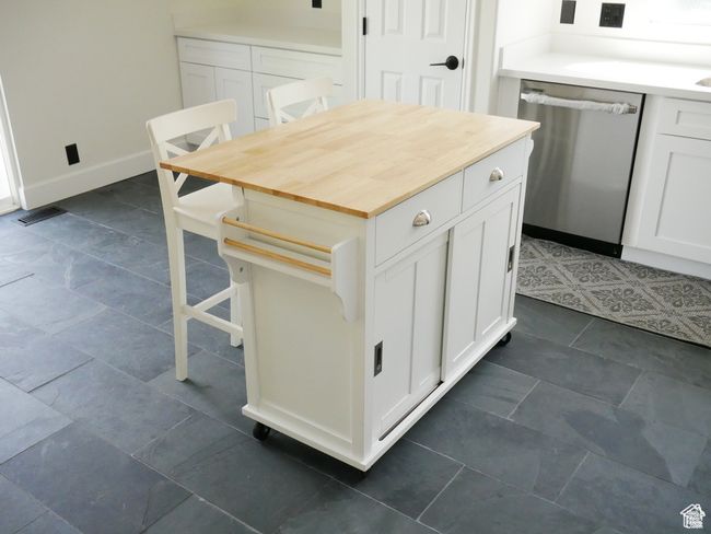 Kitchen featuring stainless steel dishwasher, white cabinets, wood counters, a kitchen breakfast bar, and a kitchen island | Image 6