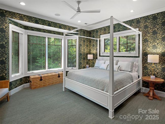 Tranquil main level primary bedroom ensuite features Serena and Lily wallpaper, luxurious Fabrica carpeting, custom wooden window blinds for light control and beautiful private wooded views. | Image 22