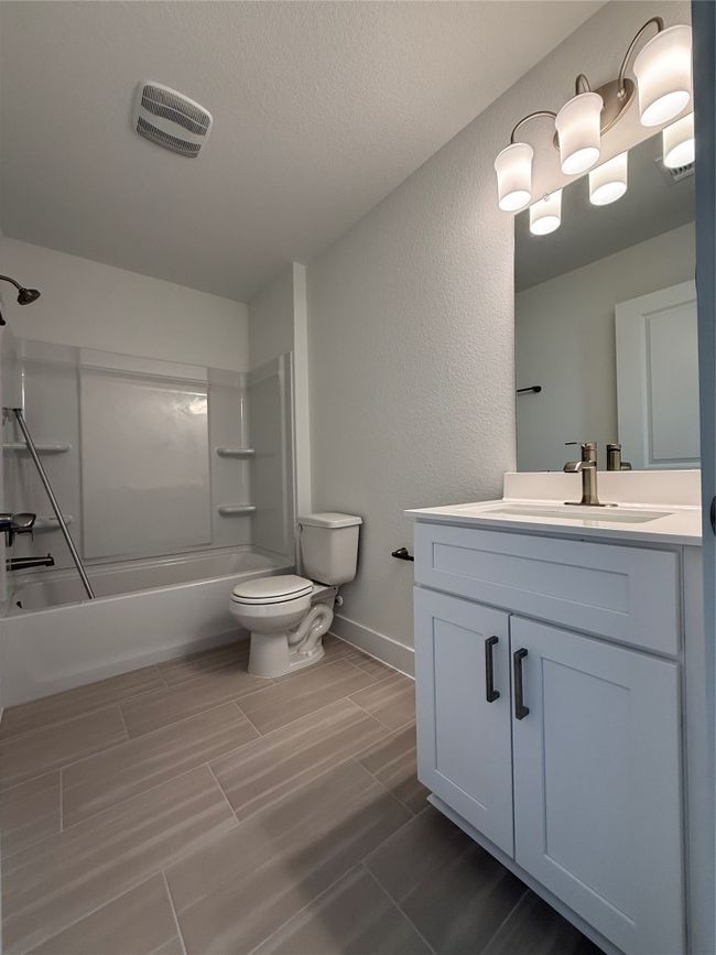 Bathroom featuring vanity, toilet, shower / bathtub combination, a textured wall, and baseboards | Image 32