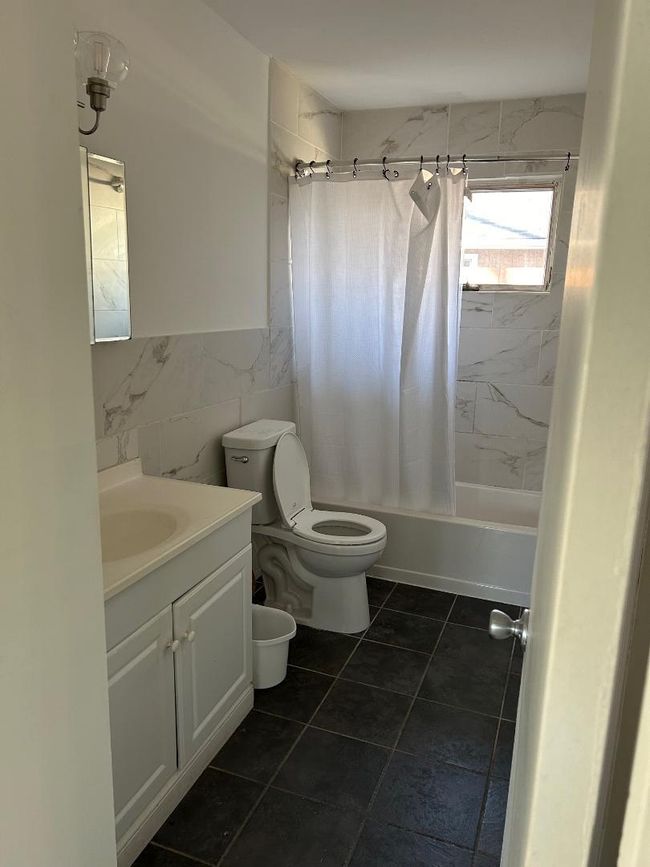 Full bathroom featuring toilet, vanity, tile walls, and shower / bathtub combination with curtain | Image 12
