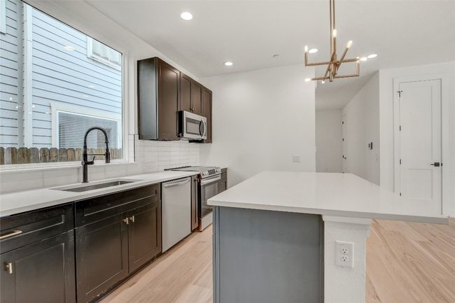 Kitchen featuring stainless steel appliances, a sink, a kitchen island, light wood finished floors, and backsplash | Image 16