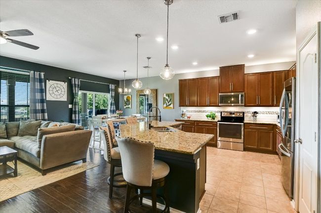 Kitchen with stainless steel appliances, a sink, open floor plan, ceiling fan, and light stone counters | Image 9