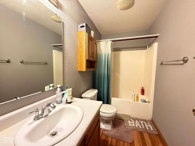 full bath with wood finished floors, a textured ceiling, vanity, and shower / bathtub combination with curtain | Image 14
