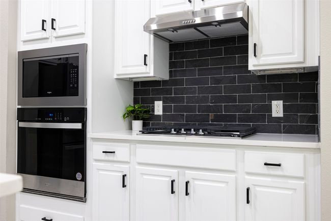 Kitchen featuring exhaust hood, gas cooktop, appliances with stainless steel finishes, backsplash, and white cabinetry | Image 6