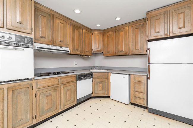 Kitchen with white appliances, light floors, light countertops, under cabinet range hood, and a sink | Image 13