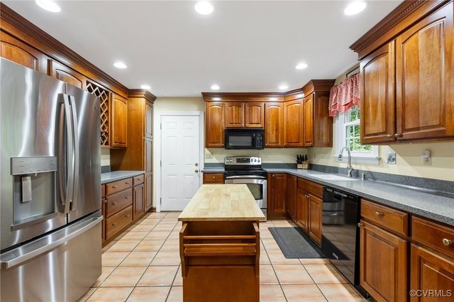 Kitchen with appliances, wood counters, light tile patterned flooring, recessed lighting, and a center island | Image 12