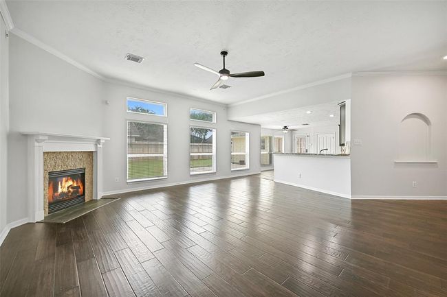 The open-concept family room flows seamlessly into the kitchen and breakfast area, with a wall of windows offering backyard views, a modern ceiling fan, and a cozy fireplace as the focal point—all set atop rich engineered wood flooring. | Image 10