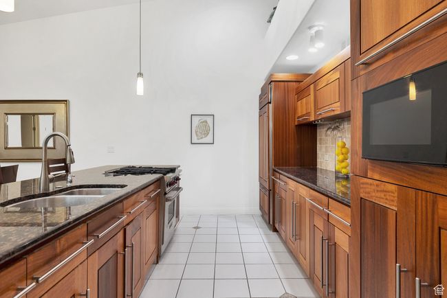 Kitchen with premium appliances, a sink, dark stone counters, decorative backsplash, and baseboards | Image 6