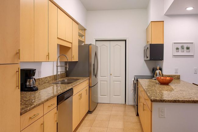 Kitchen featuring stainless steel appliances, light brown cabinets, dark stone counters, and light tile patterned floors | Image 12