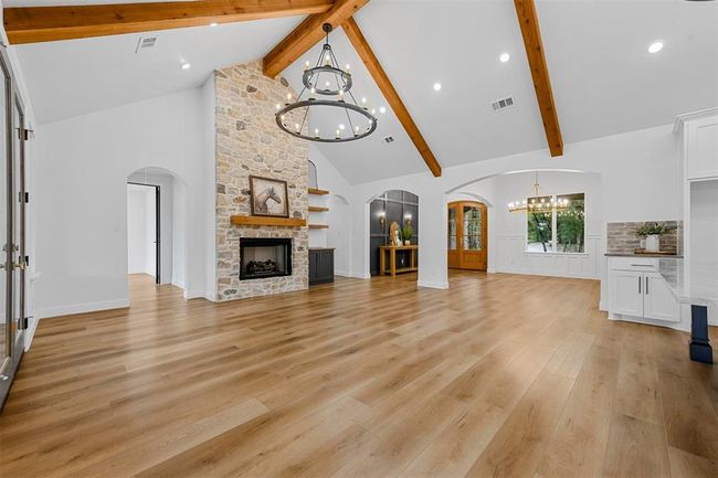 Unfurnished living room with high vaulted ceiling, light hardwood / wood-style floors, beam ceiling, and a stone fireplace | Image 7