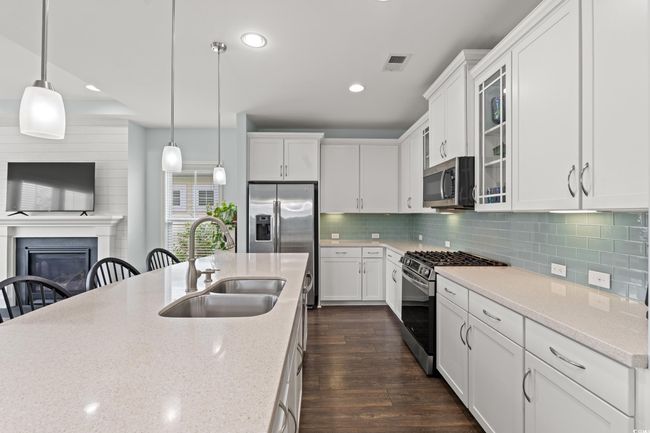 Kitchen with appliances with stainless steel finishes, a sink in the large island, dark wood-style flooring, glass insert cabinets, light stone counters, recessed lighting and under cabinet lighting. | Image 27