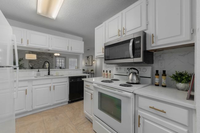 Kitchen featuring white cabinets, backsplash, light countertops, a sink, and white appliances | Image 19