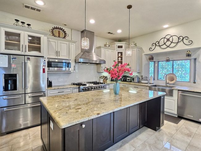 Kitchen featuring appliances with stainless steel finishes, wall chimney range hood, a sink, a kitchen island, and glass insert cabinets | Image 11