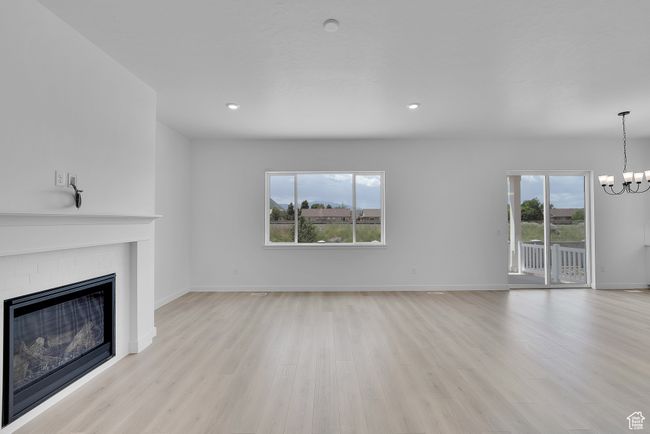 Unfurnished living room featuring a chandelier, light wood-type flooring, a fireplace, baseboards, and recessed lighting | Image 5