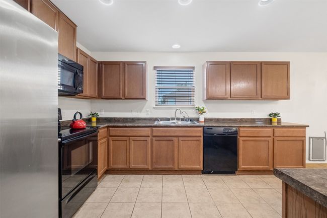 Kitchen featuring black appliances, dark countertops, a sink, and light tile patterned flooring | Image 9