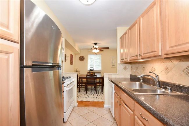 Kitchen featuring white appliances, light brown cabinets, dark countertops, light tile patterned floors, and a ceiling fan | Image 16