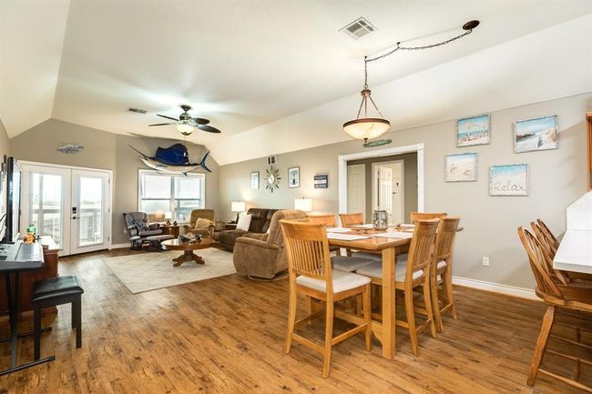 This spacious open-concept living and dining area features warm wood flooring, neutral walls, and ample natural light. It includes a cozy seating area, dining table, and a bar-style counter, perfect for entertaining. Decorated with coastal-themed accents, it offers a relaxed, inviting atmosphere. | Image 7