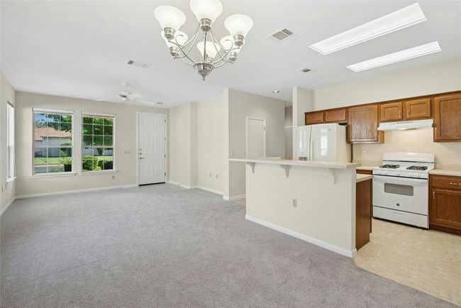 Kitchen with white appliances, under cabinet range hood, a kitchen breakfast bar, light carpet, and light countertops | Image 9