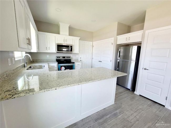 Kitchen with appliances with stainless steel finishes, light stone counters, a peninsula, white cabinetry, and light wood finished floors | Image 6