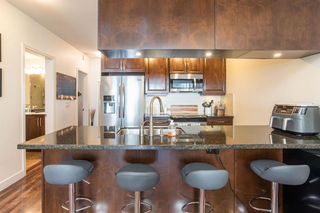 Kitchen featuring dark wood-style floors, a kitchen breakfast bar, a sink, and stainless steel appliances | Image 5