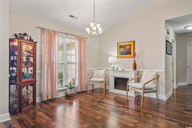 Living area with wood finished floors, a chandelier, a glass covered fireplace, and lofted ceiling | Image 6