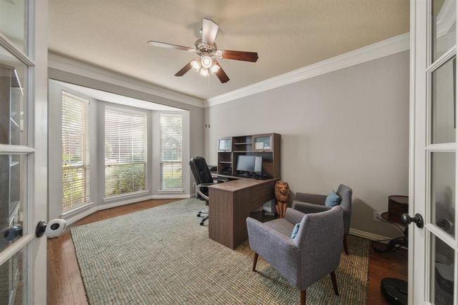 Opposite the formal dining room and accessible via French doors is a private study with crown moulding, a ceiling fan with lighting, windows with blinds & hardwood floors. | Image 8
