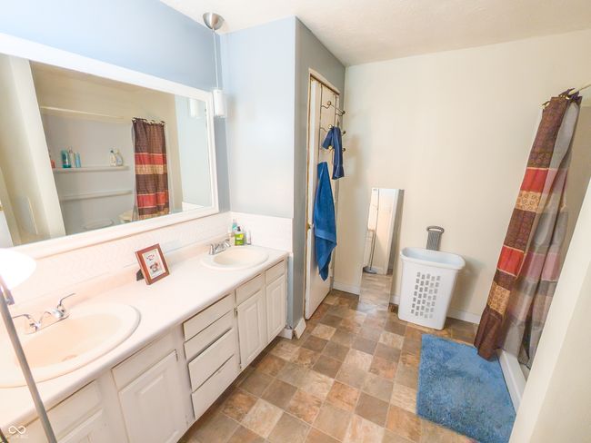 bathroom featuring stone finish flooring, double vanity, baseboards, and a shower with shower curtain | Image 7
