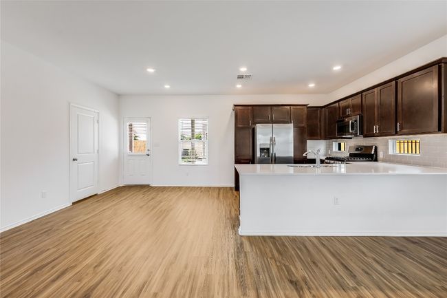 Kitchen with stainless steel appliances, light wood-type flooring, dark brown cabinetry, a peninsula, and light countertops | Image 9