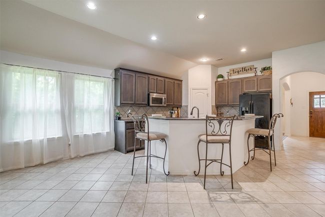 Kitchen featuring stainless steel microwave, black refrigerator with ice dispenser, arched walkways, backsplash, and vaulted ceiling | Image 13