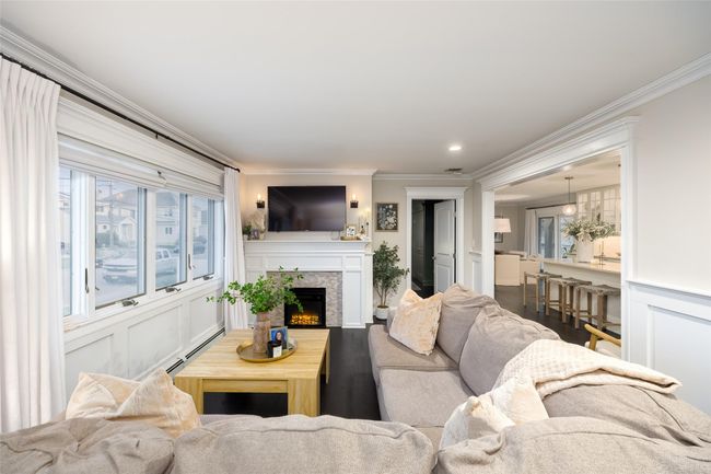 Living area featuring a lit fireplace, wood finished floors, a baseboard radiator, and crown molding | Image 13